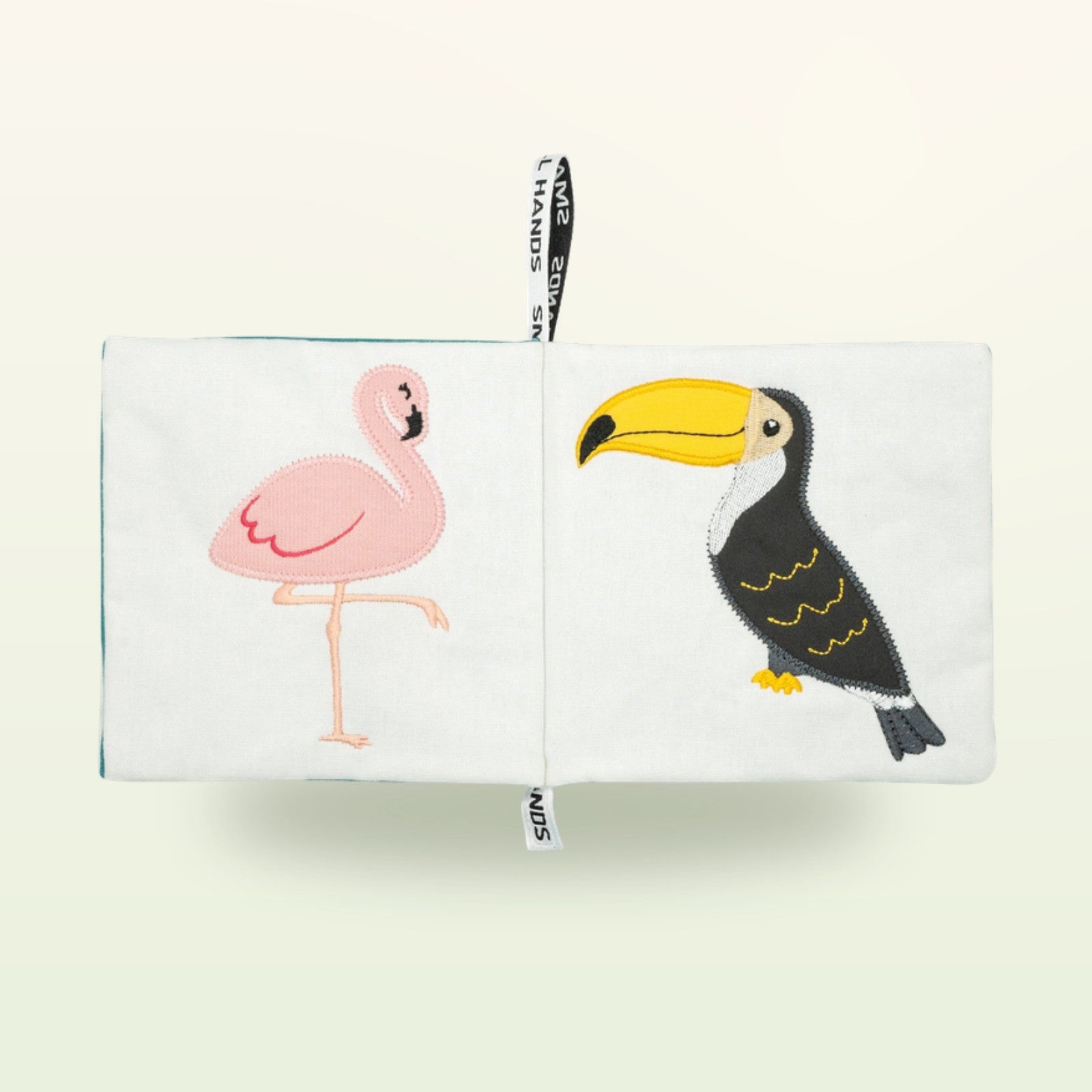 Small Hands Vögel Montessori Stoffbuch aufgeschlagen – rosa Flamingo und Tukan auf sanftem Creme-Hintergrund – ab 0 Monaten