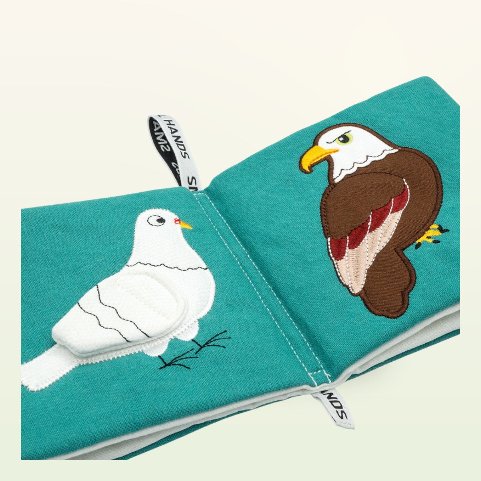 Small Hands Vögel Montessori Stoffbuch aufgeschlagen – weiße Taube und Adler in Schrägansicht auf sanftem Creme-Hintergrund – ab 0 Monaten