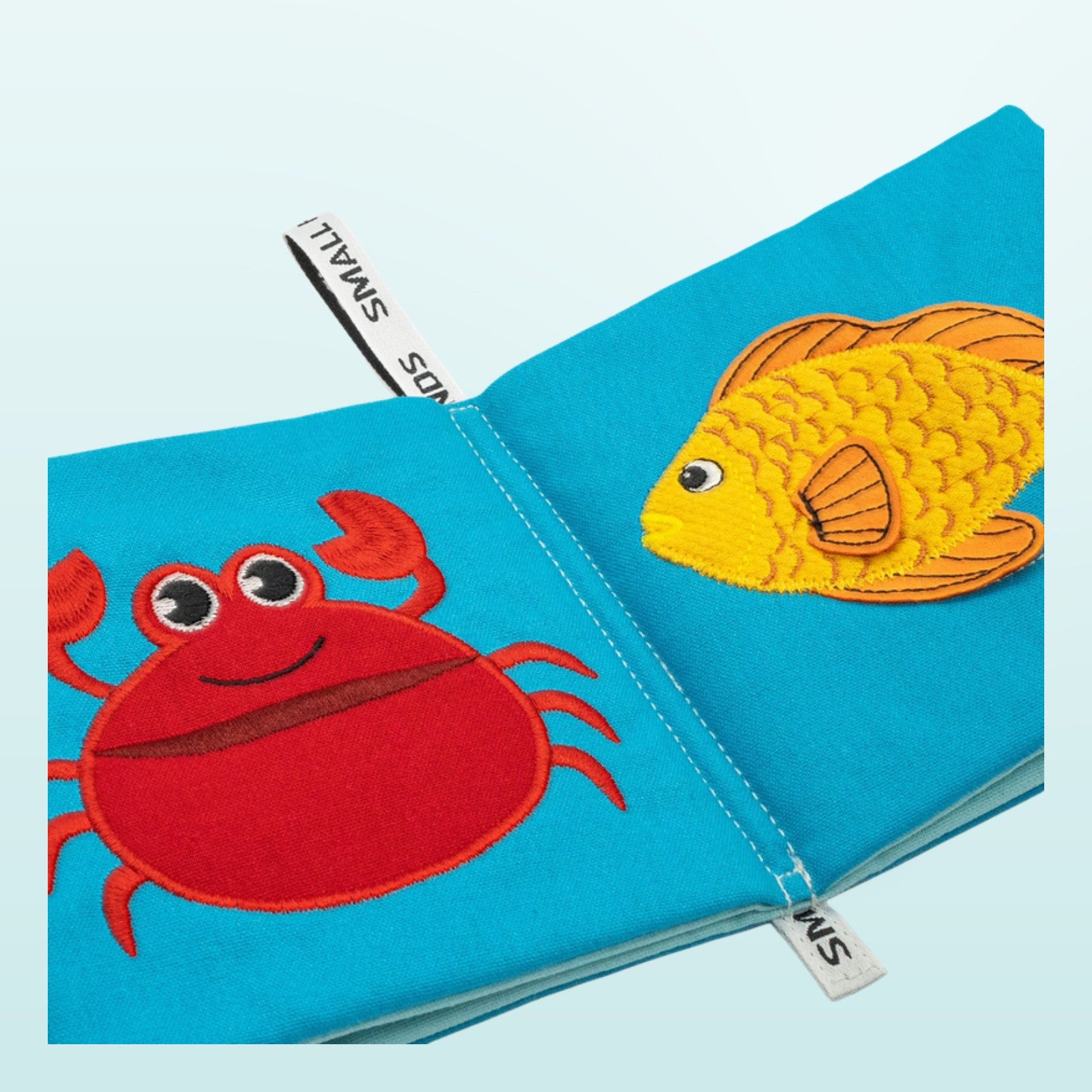 Small Hands Meeresbewohner Montessori Stoffbuch Nahaufnahme mit Krabbe und Goldfisch auf sanftem Unterwasser-Blau-Hintergrund – ab 1 Jahr